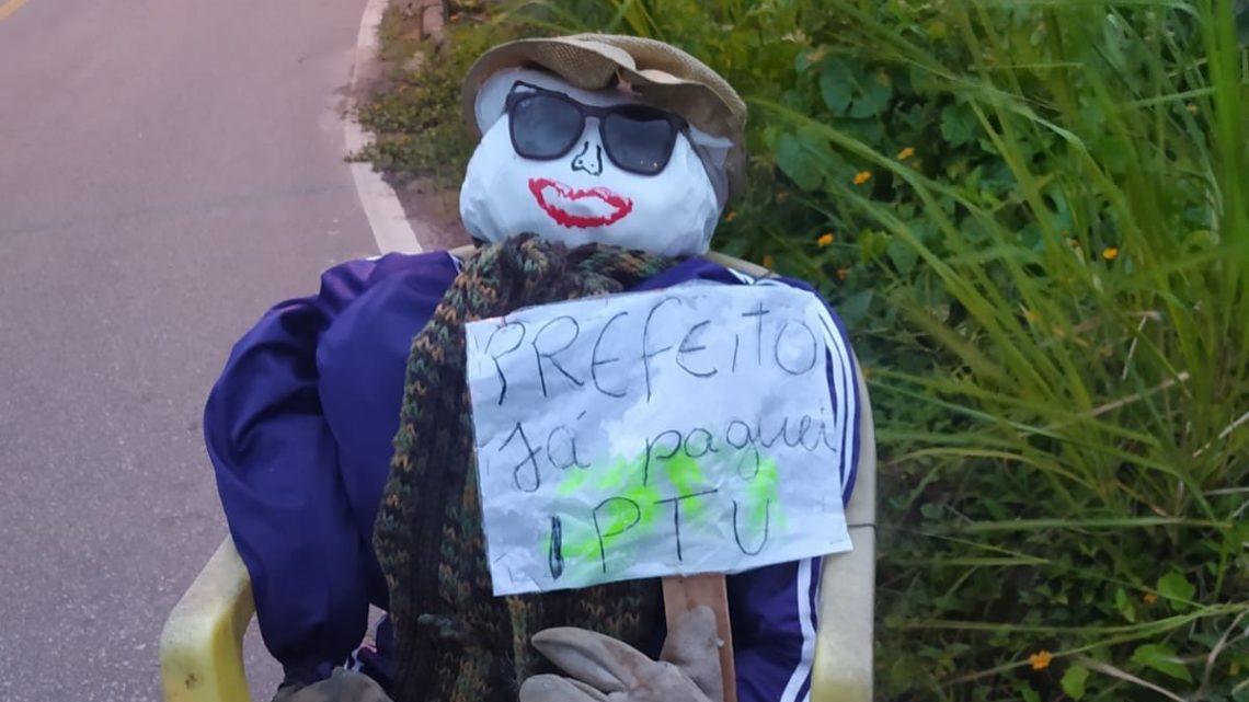 “Já paguei meu IPTU”: morador usa boneco e cartaz para cobrar obras em rua de SC